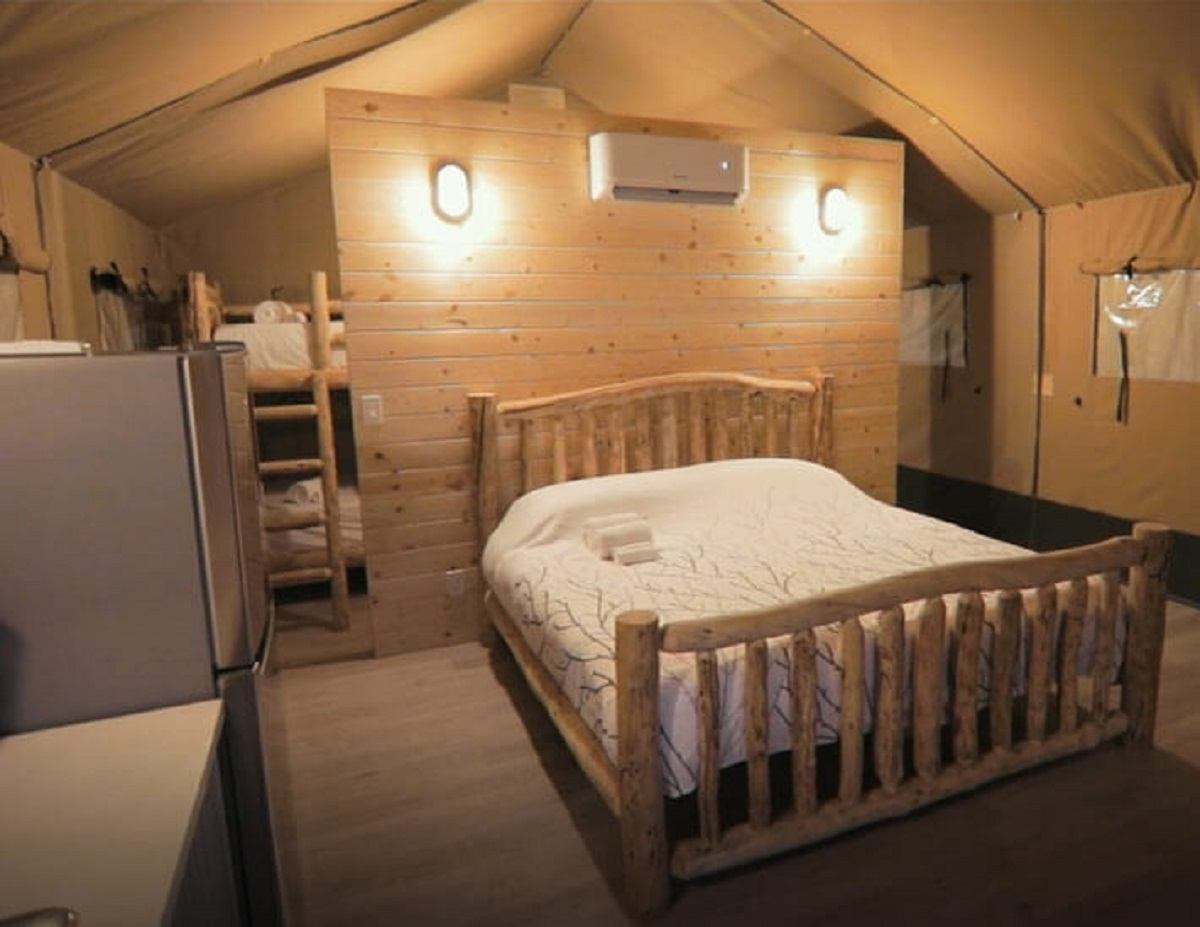 Rustic glamping tent interior with wooden bed, bunk beds, and cozy lighting.