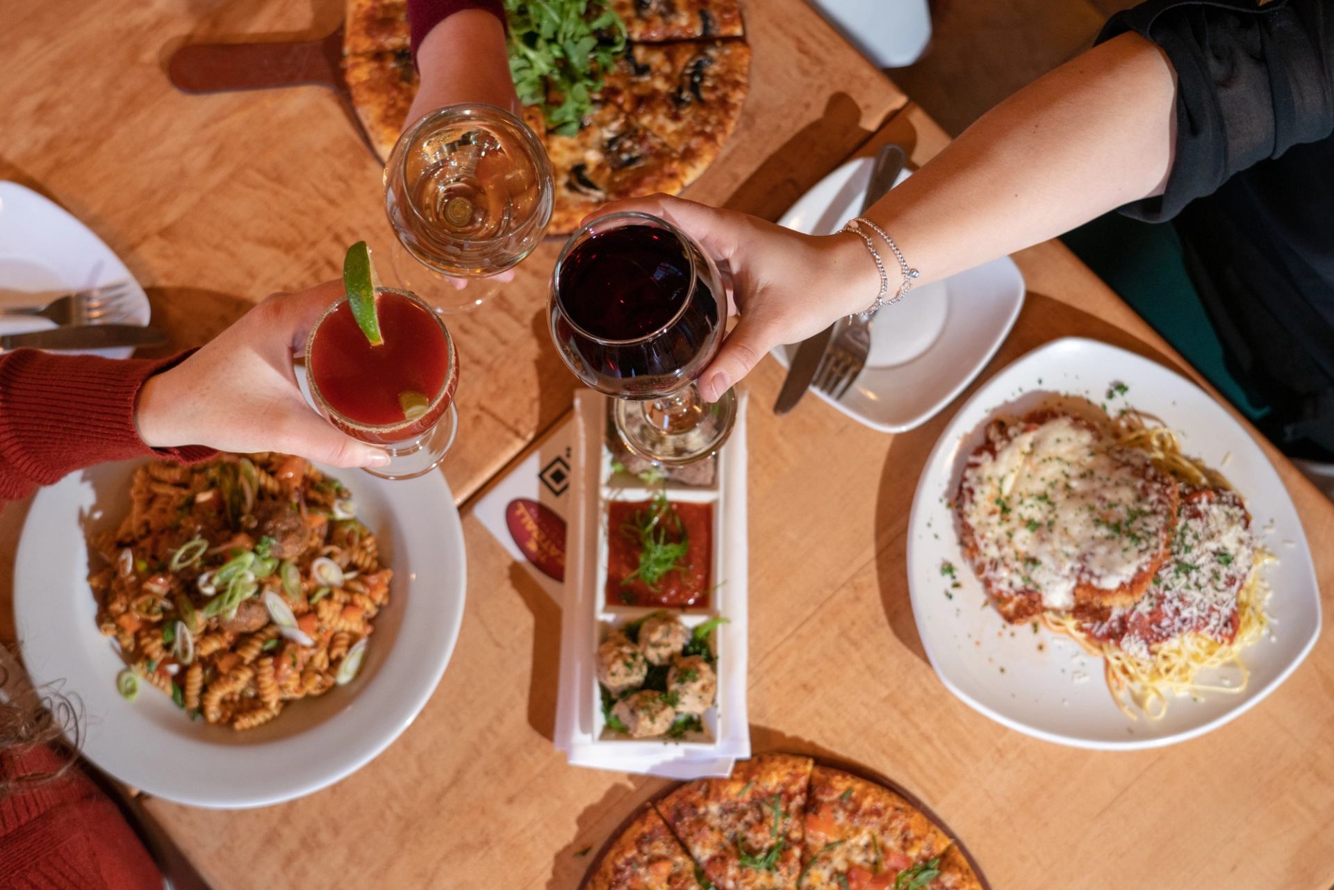 Table with pizza, pasta, meatballs, appetizers, and drinks in a cozy dining setting.
