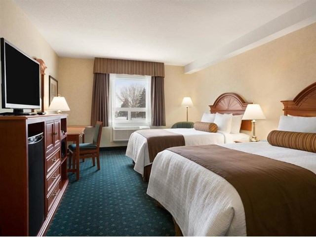 Hotel room with two beds, desk, TV, and window overlooking trees.