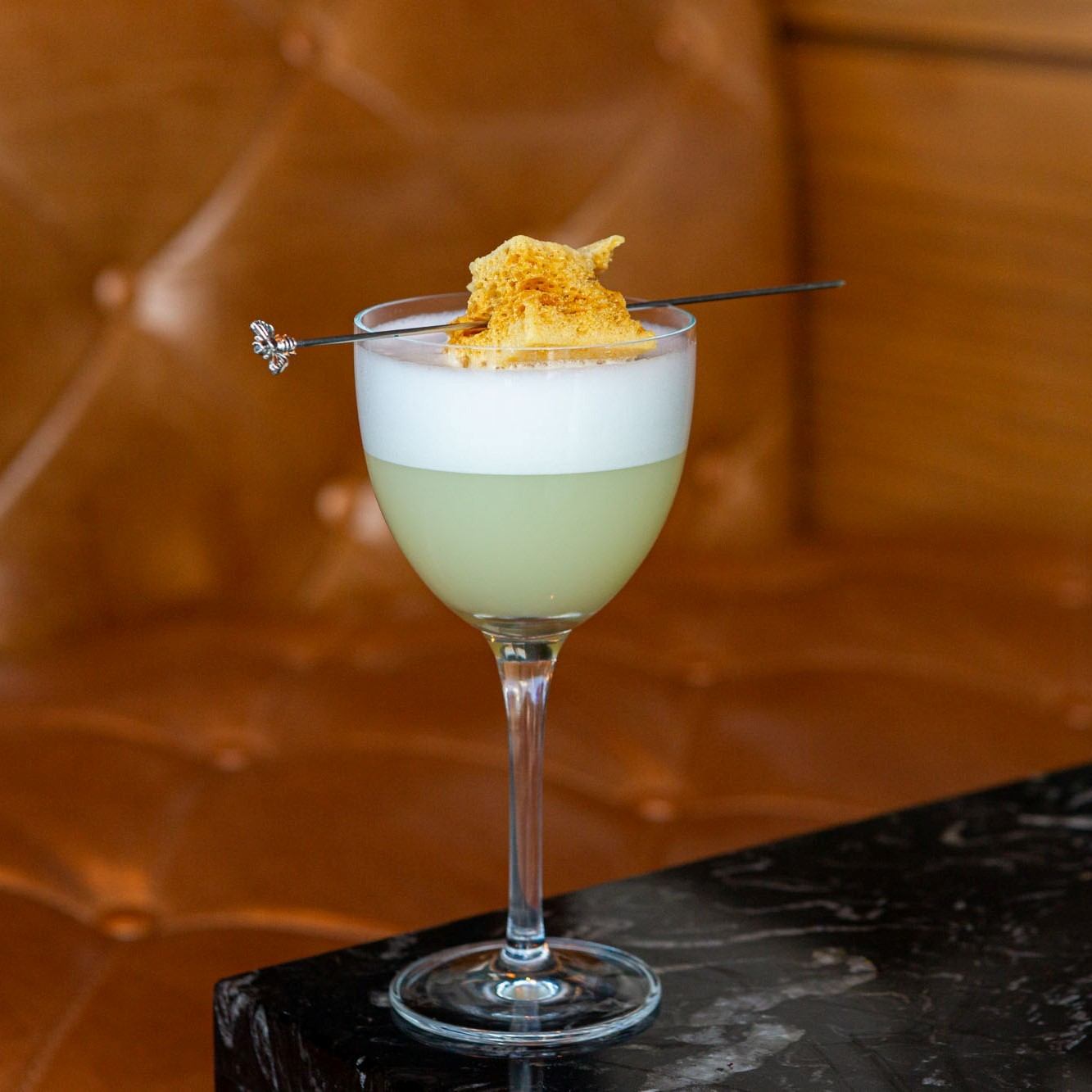 Green cocktail with foam and garnish on a skewer in a stemmed glass