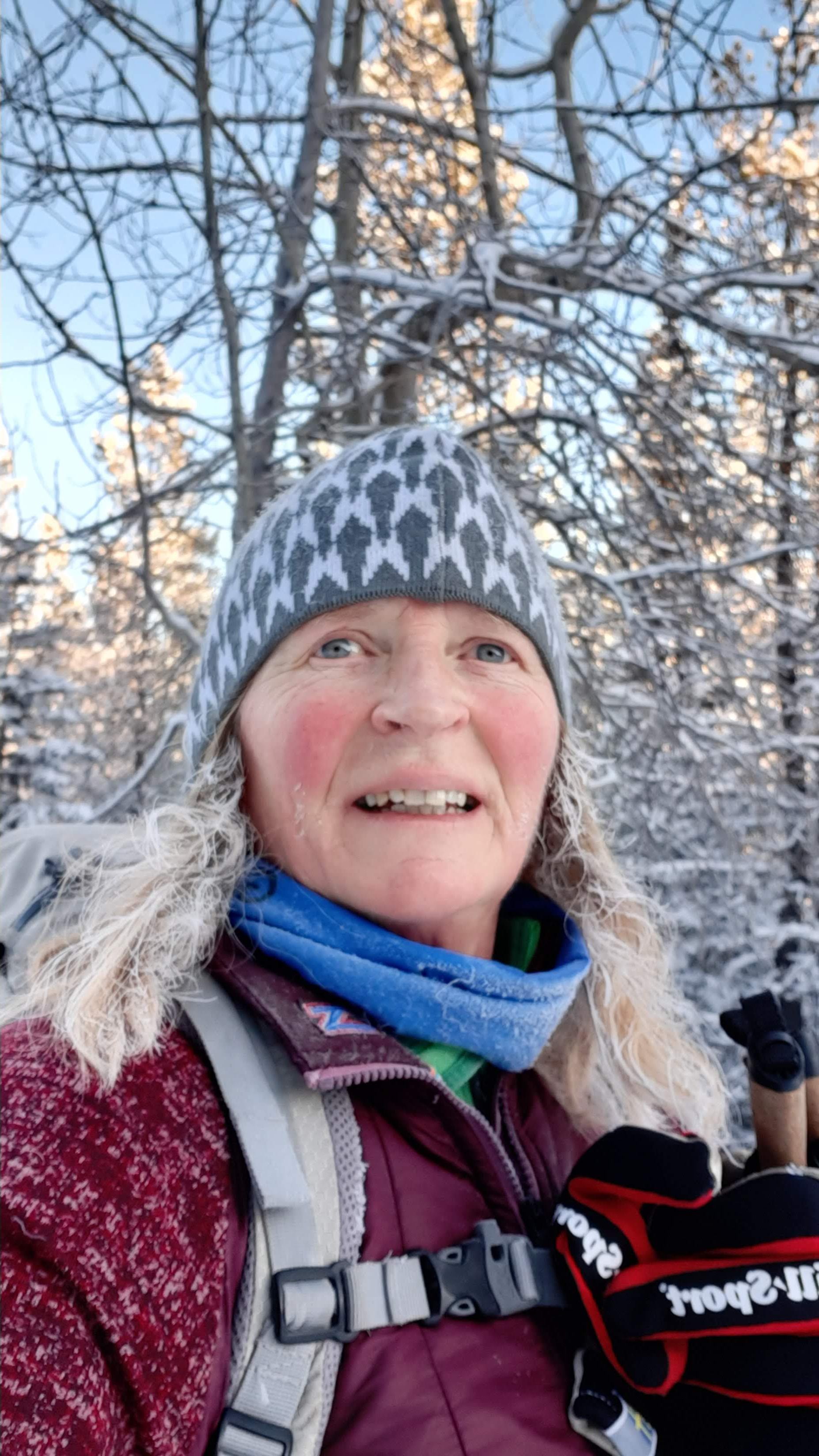 Person in winter gear stands in snowy forest under clear blue sky.