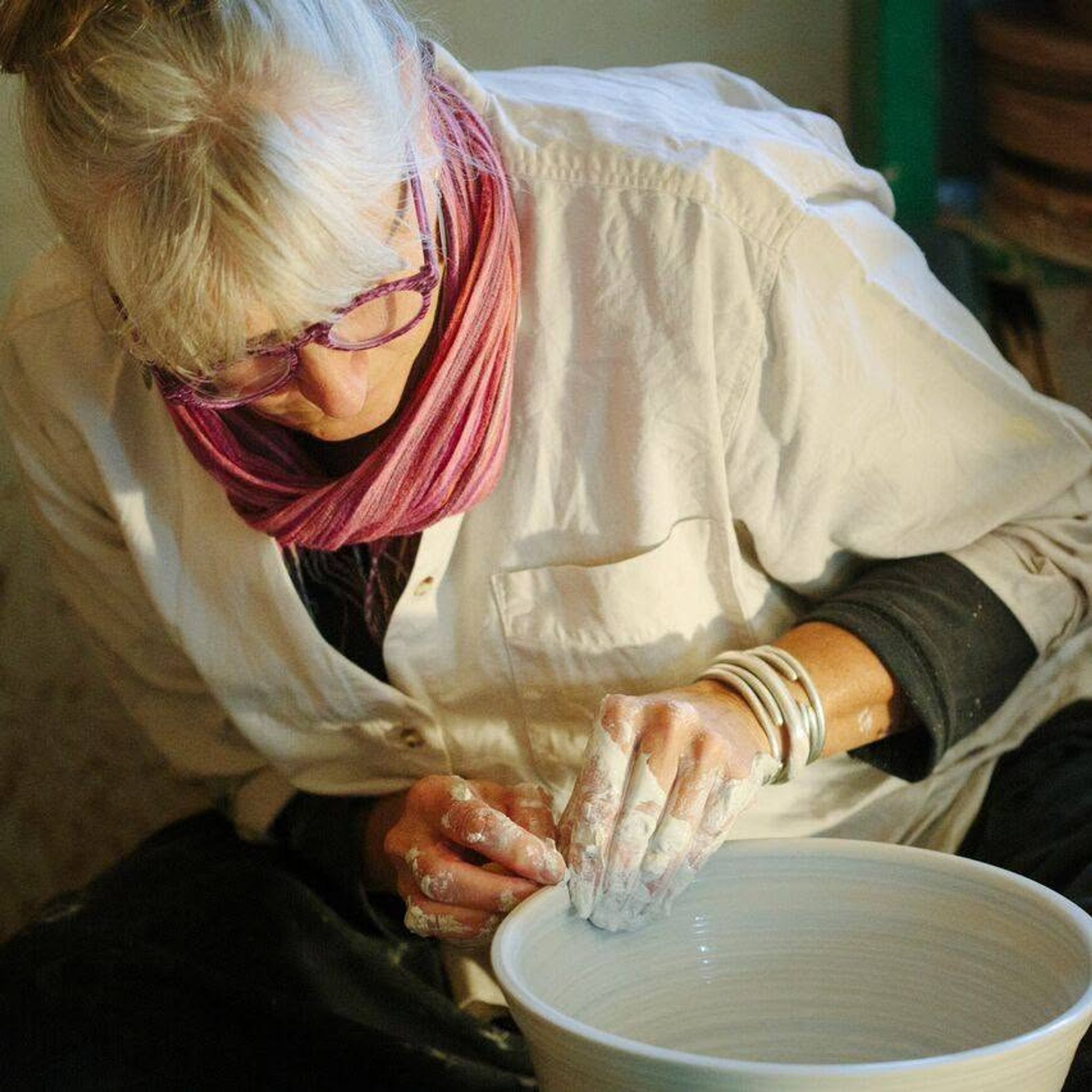 Potter with flour-dusted hands shaping a clay bowl on a pottery wheel indoors.
