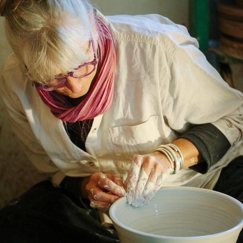 Potter with flour-dusted hands shaping a clay bowl on a pottery wheel indoors.