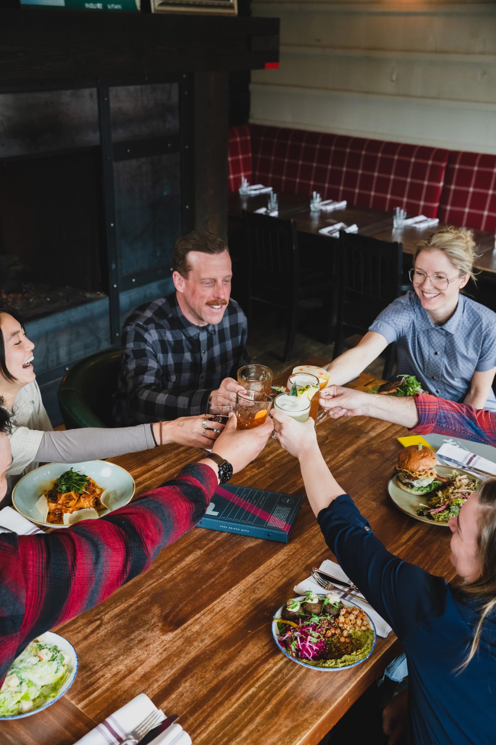 A group raising their drinks over a table filled with burgers, salads, and shared dishes.