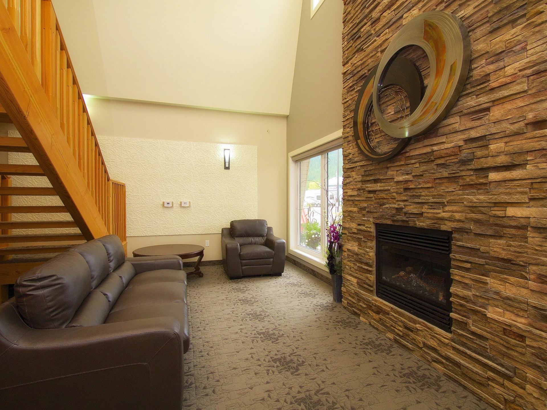 Lobby with leather seating, wooden staircase and fireplace set in a stone wall.