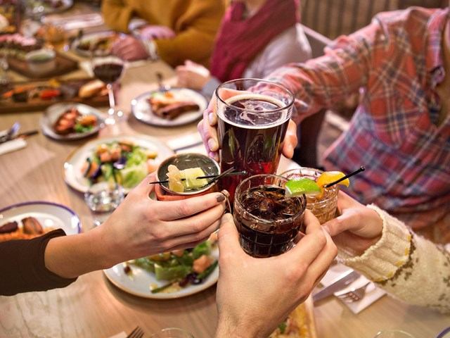 People toasting drinks over a dinner table with food and drinks in front of them.