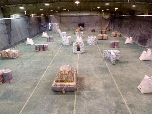 Indoor paintball field with inflatable bunkers, netted walls and overhead lights.