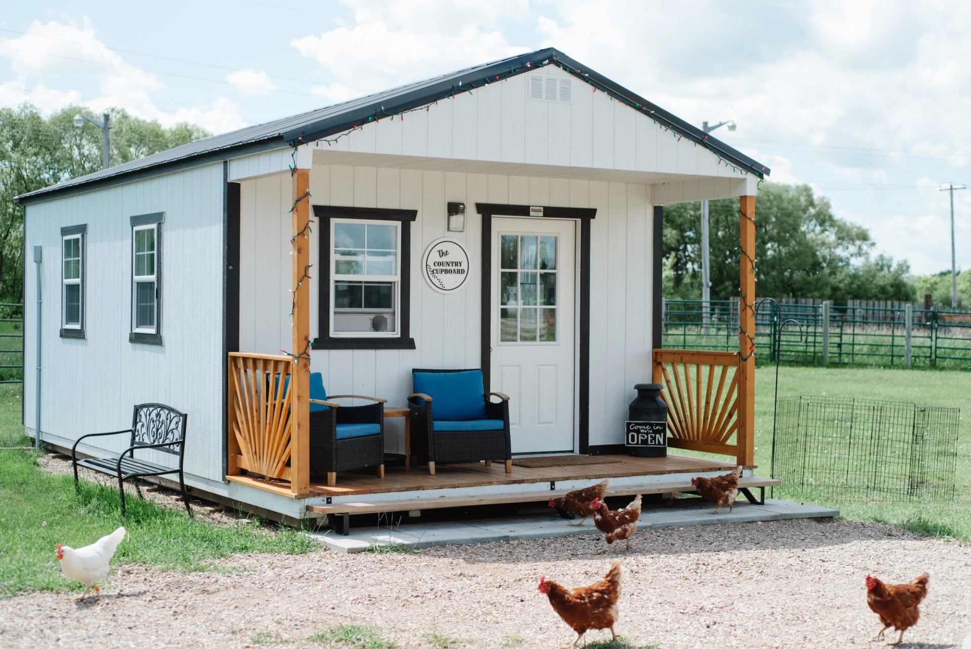 Small white farm shop with porch seating and chickens walking in front.
