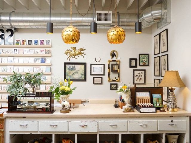 Artisan shop display with framed photos, shelves, lamp, floral arrangements, and decorative hanging .