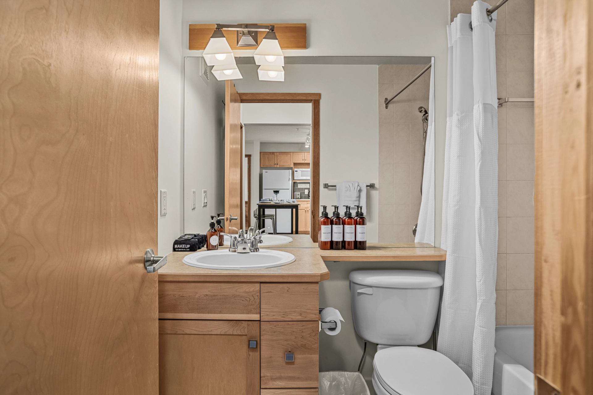 Bathroom with wood vanity, large mirror, toilet and white shower curtain.