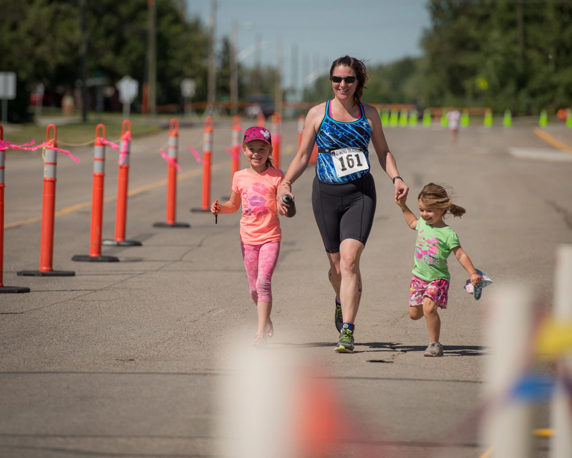 Runner wearing bib 161 jogs on road while holding hands with two children.