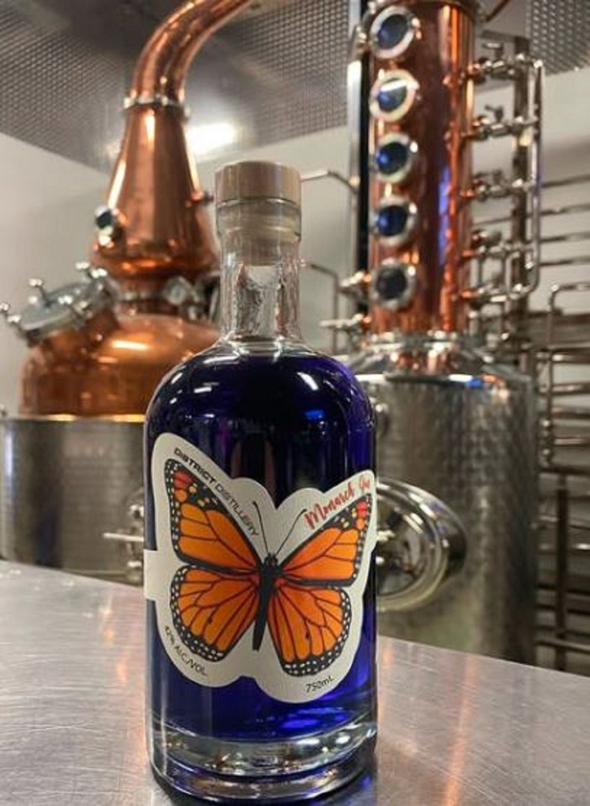 A bottle of Monarch Gin with the copper still behind it.