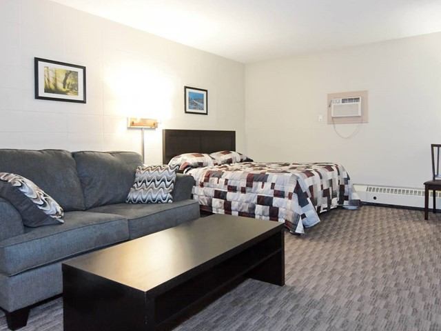 Cozy motel room with sofa, coffee table, and two beds with patchwork quilts.