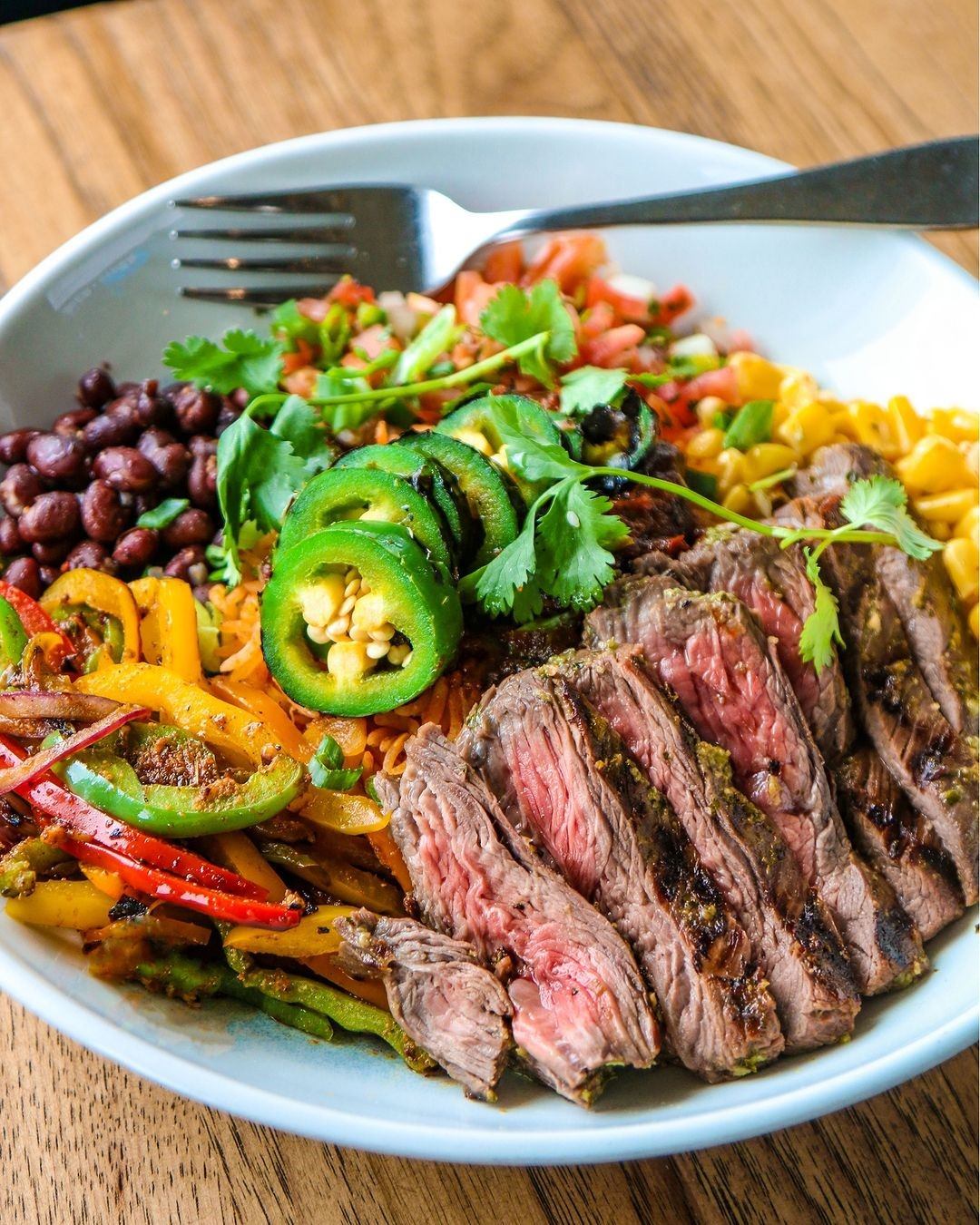 Bowl with steak, beans, veggies, and herbs served with a fork.