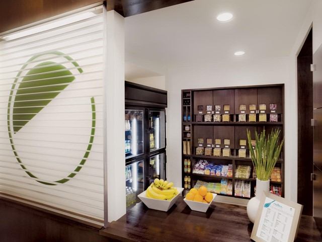 Hotel snack area with fruit bowls, drinks fridge, and shelves of packaged snacks.