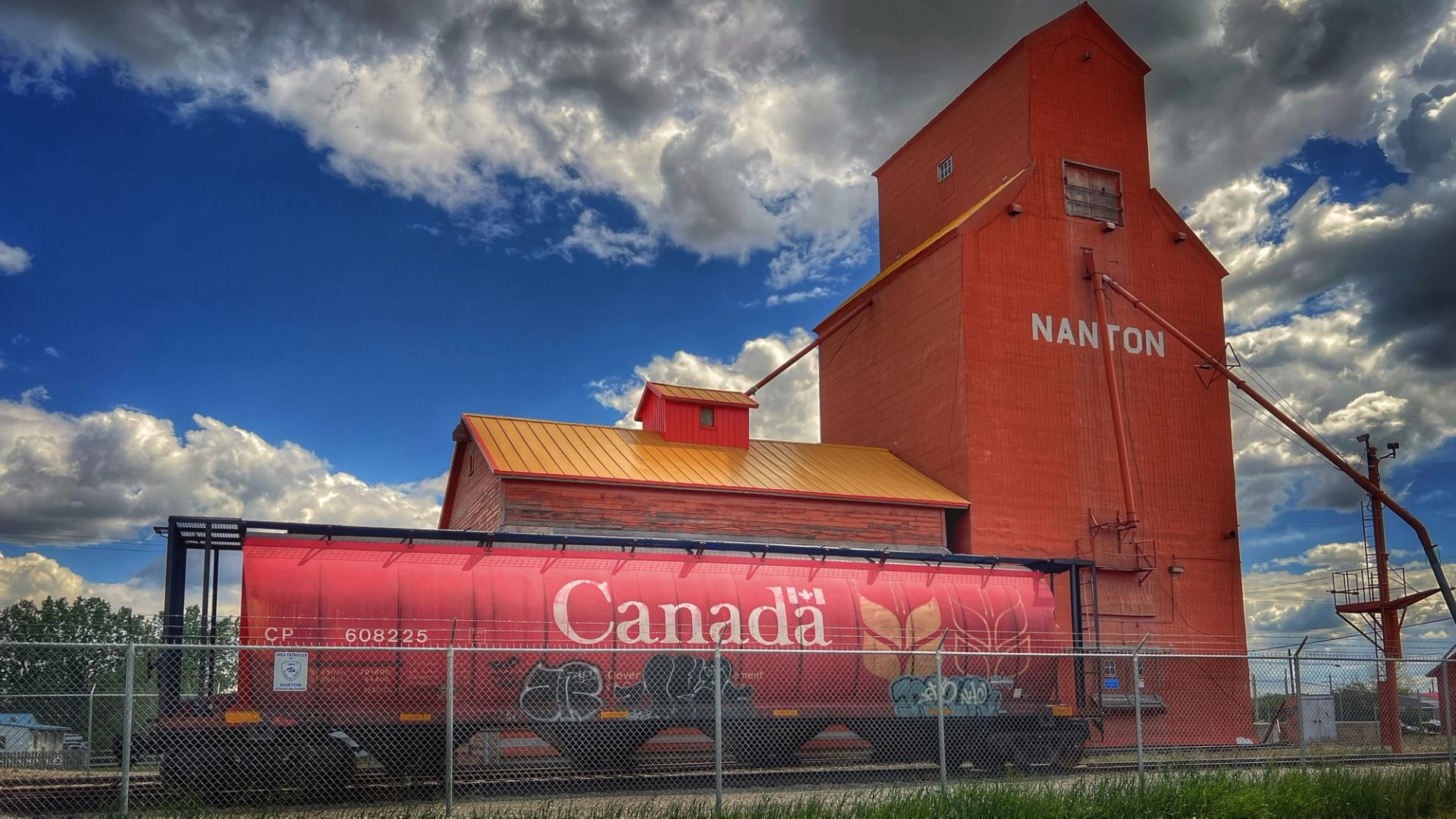 Red grain elevator and bright rail car beneath dramatic clouds.