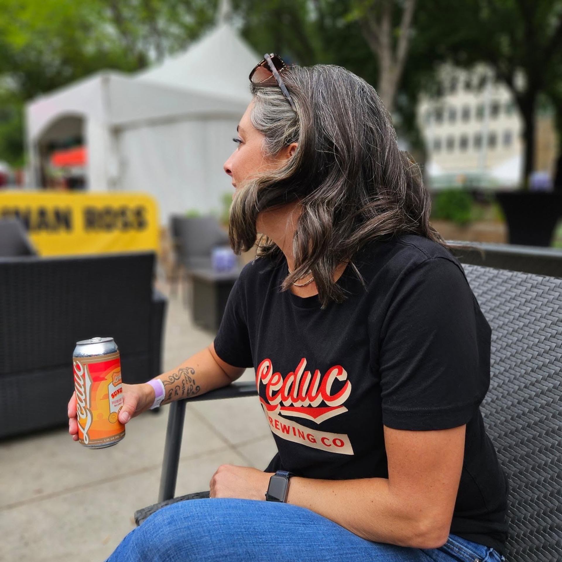 A person sits on an outdoor patio holding a beverage can during a community gathering in a park.
