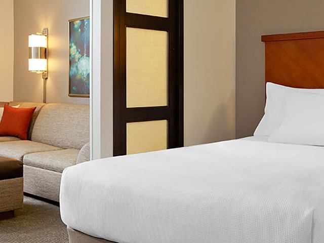 Hotel room with white linens, beige sofa, and warm lighting.