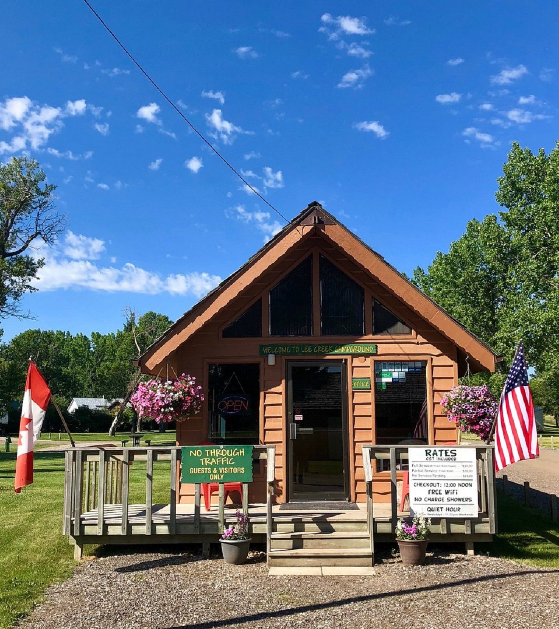 Small campground office cabin with flags, flower baskets and posted signs at entrance.