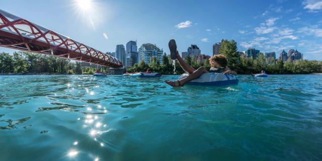 People floating down the Bow River by the Peace Bridge with a cityscape in the background in Calgary.