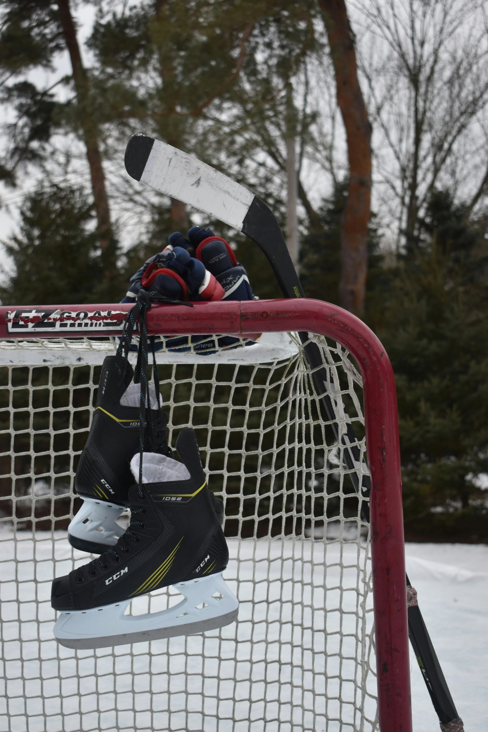 Hockey skates, gloves and stick resting on a red goal net outdoors.