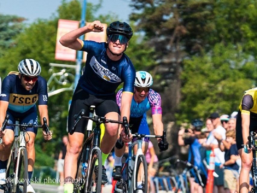 Cyclists sprint toward the finish line as a rider raises a fist near spectators.