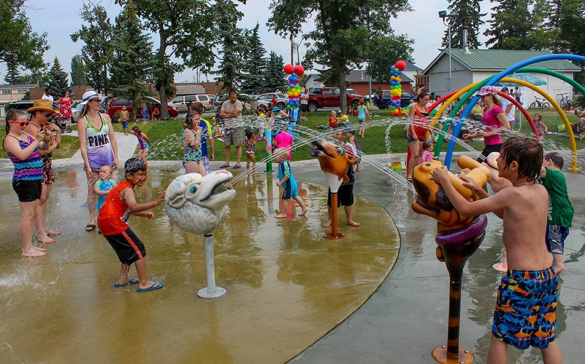 Kids playing in water at Olds Splashpark with colorful sprayers and arches.