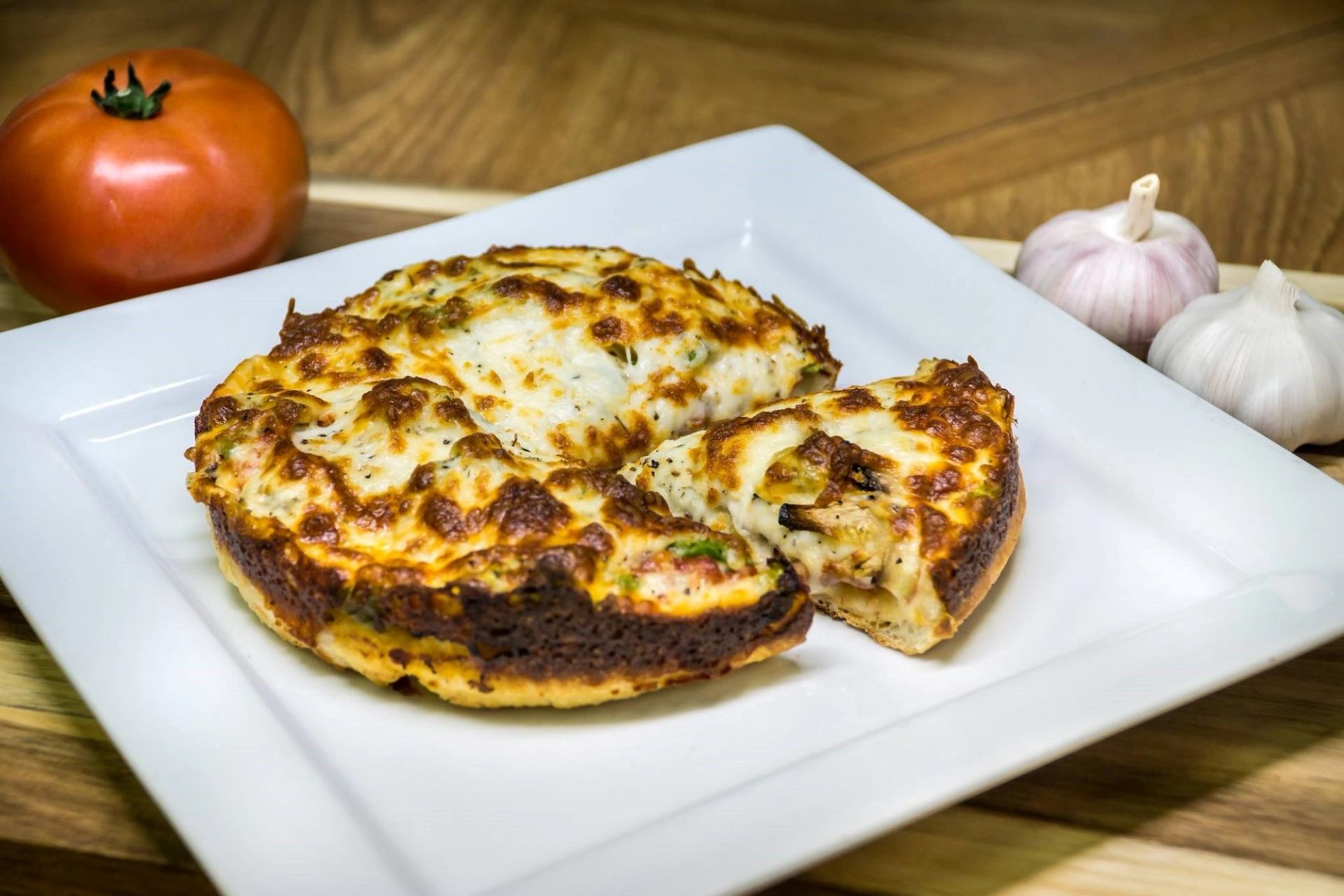Cheese pizza slices on a white plate with tomatoes and garlic on wood background.