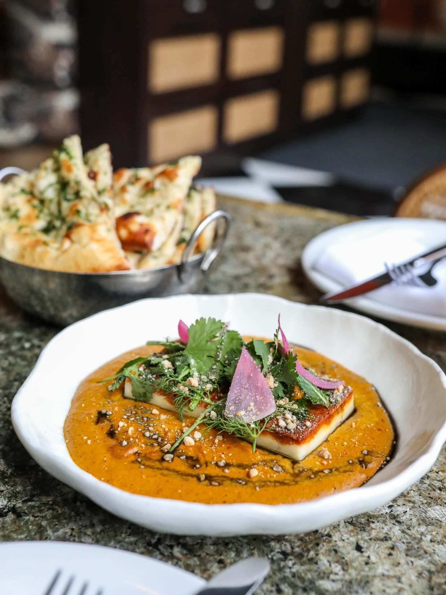 Paneer in orange curry sauce topped with herbs and onions, with naan in background.