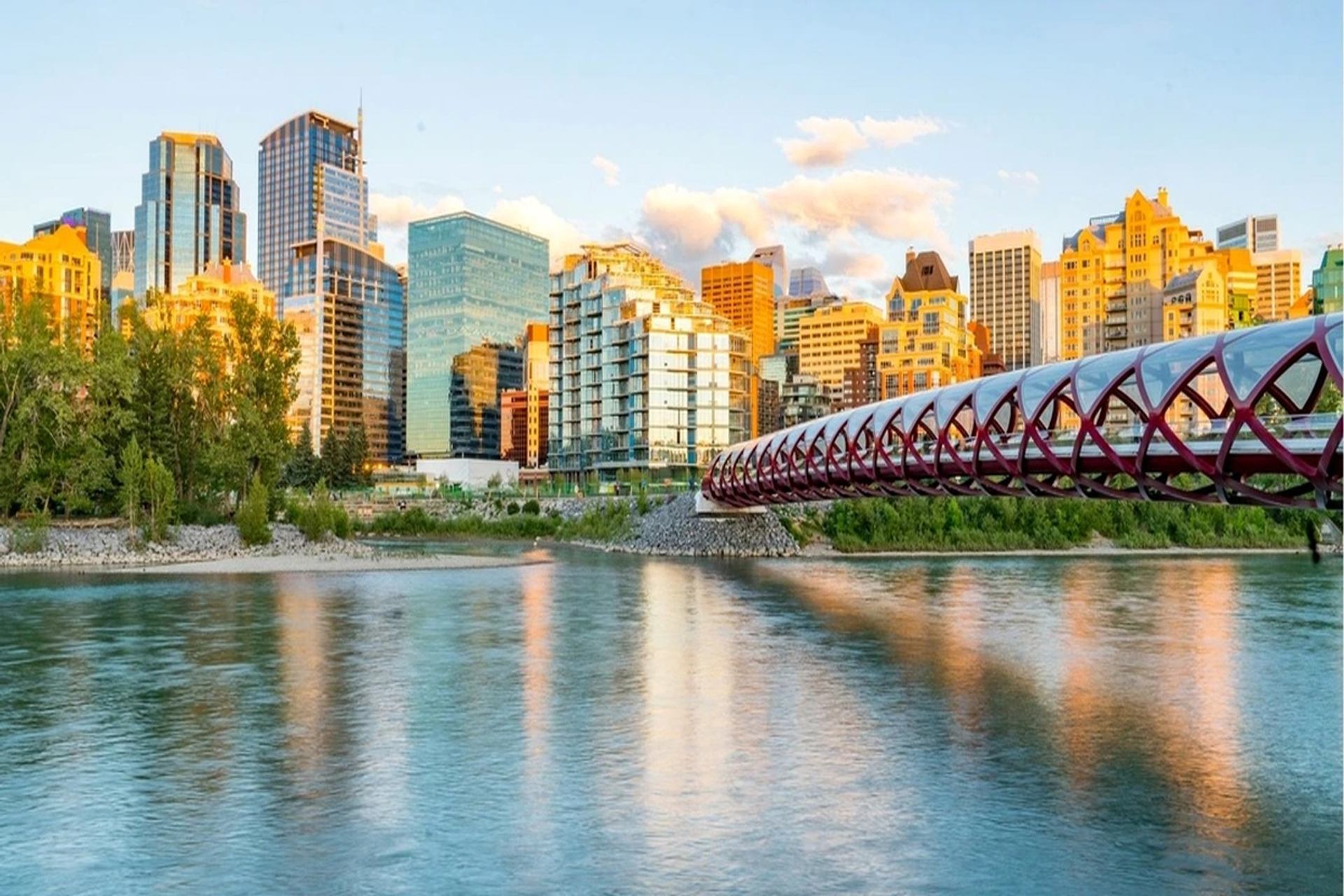 Red lattice bridge spans a river beside a skyline of modern and historic buildings.