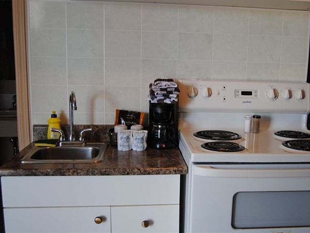 Motel kitchen with sink, stove, coffee maker, and countertop essentials.