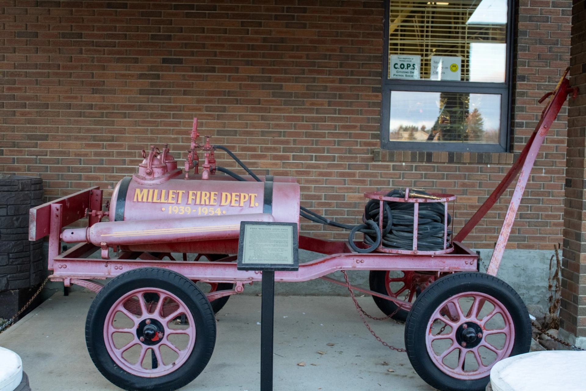 Historic Millet Fire Dept hose cart with red wheels displayed outside the museum.