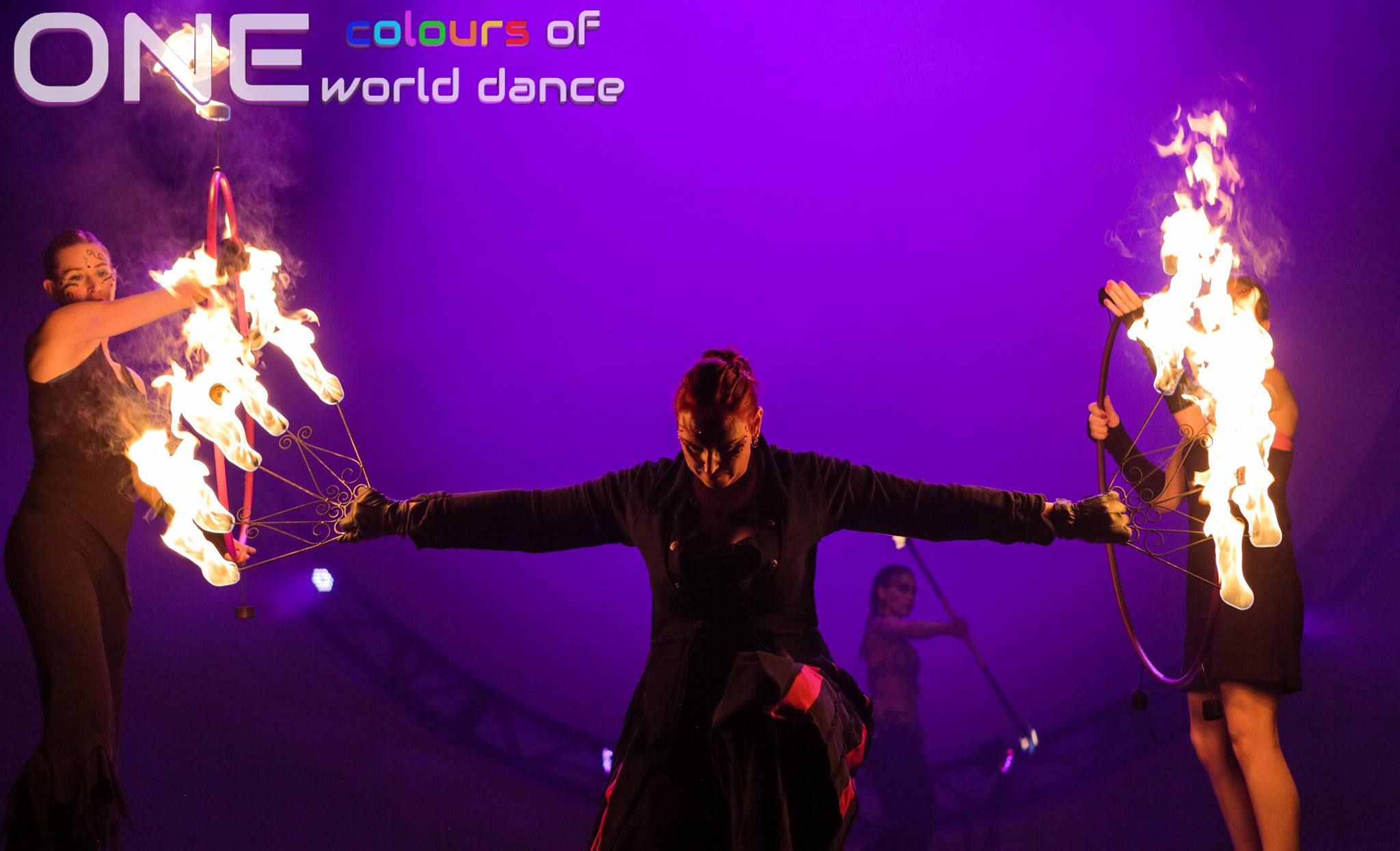 Fire dancers perform with flaming hoops onstage under purple lighting, with ONE logo above.
