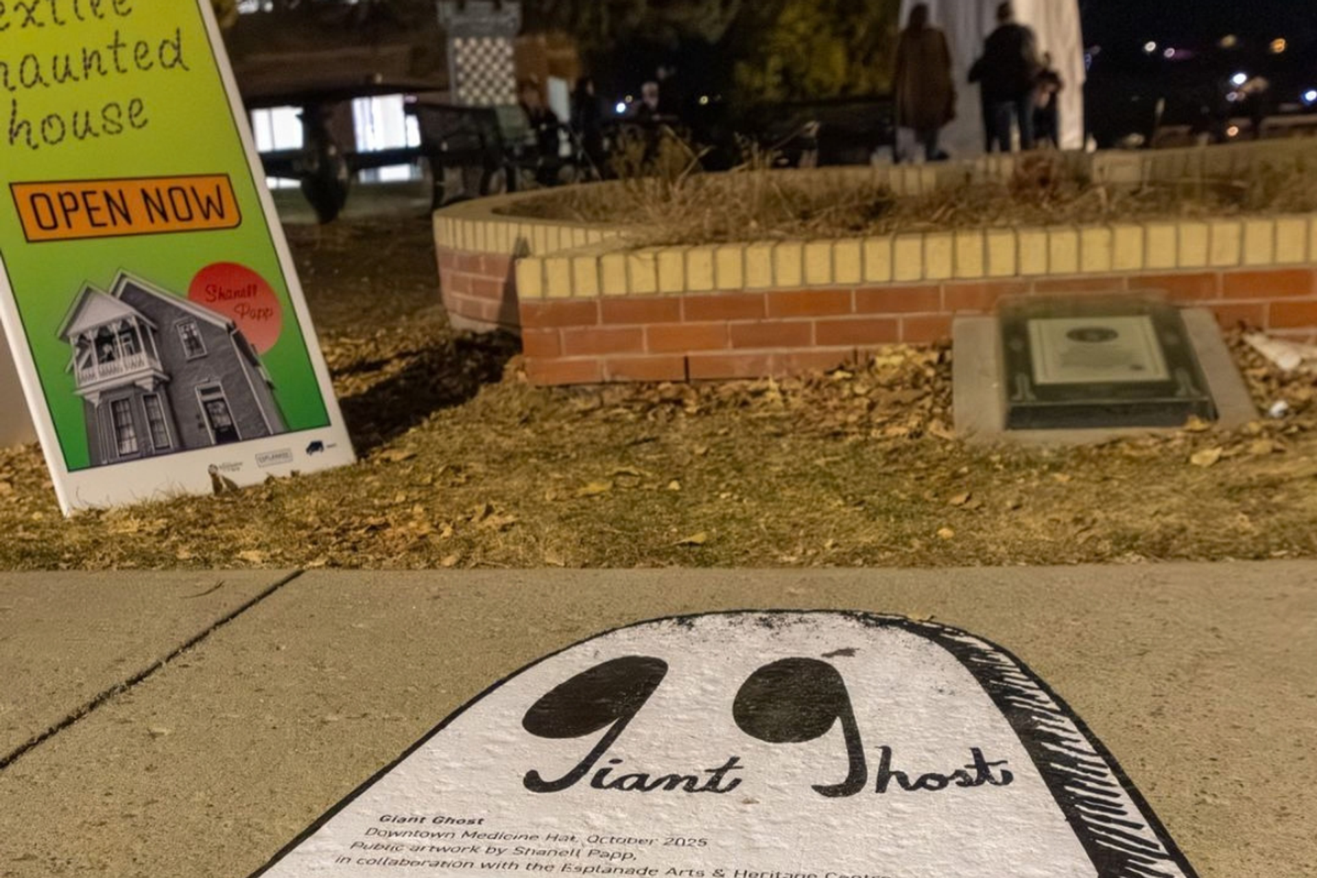 Giant Ghost sidewalk artwork beside a sign advertising an open haunted house.