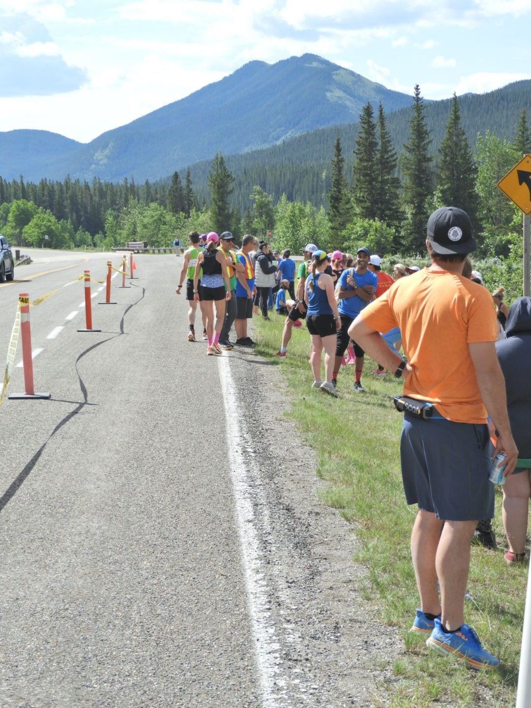 Runners line up along a mountain road during a relay race, spectators on roadside.