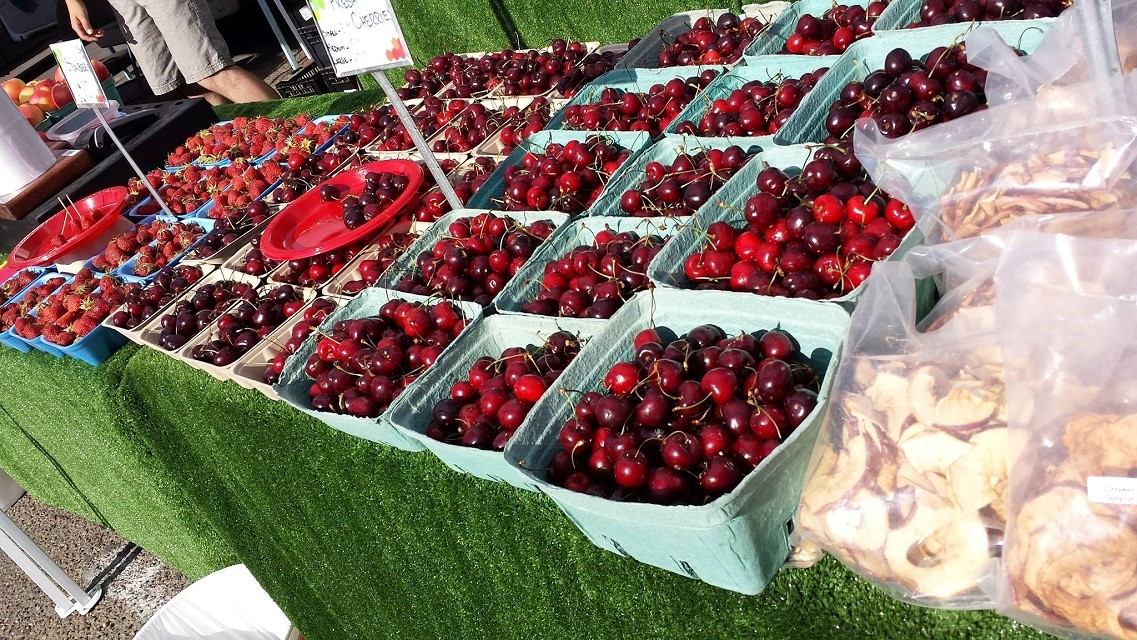 Green baskets filled with ripe cherries and bags of dried fruit on a vendor table.