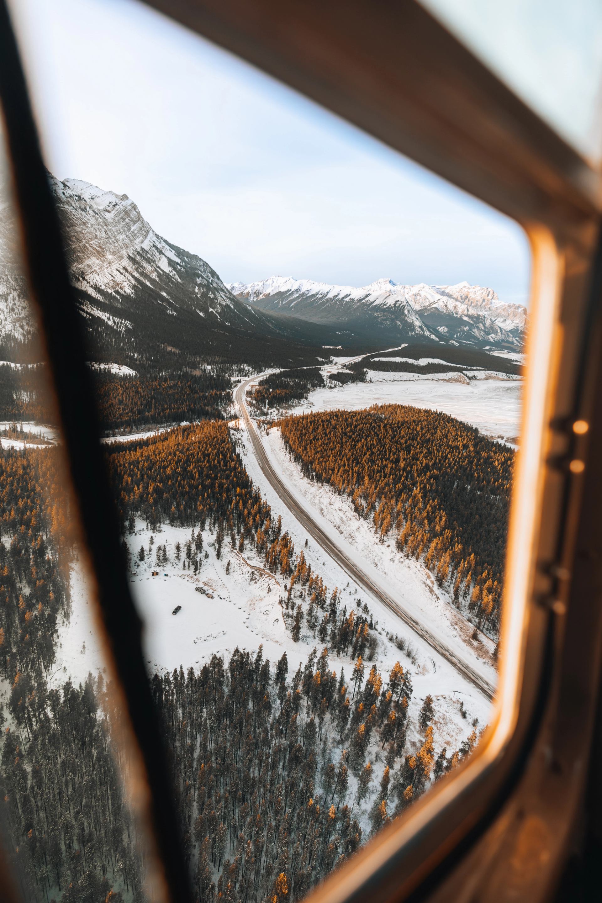 Helicopter window view of a winding road through a snowy mountain valley.