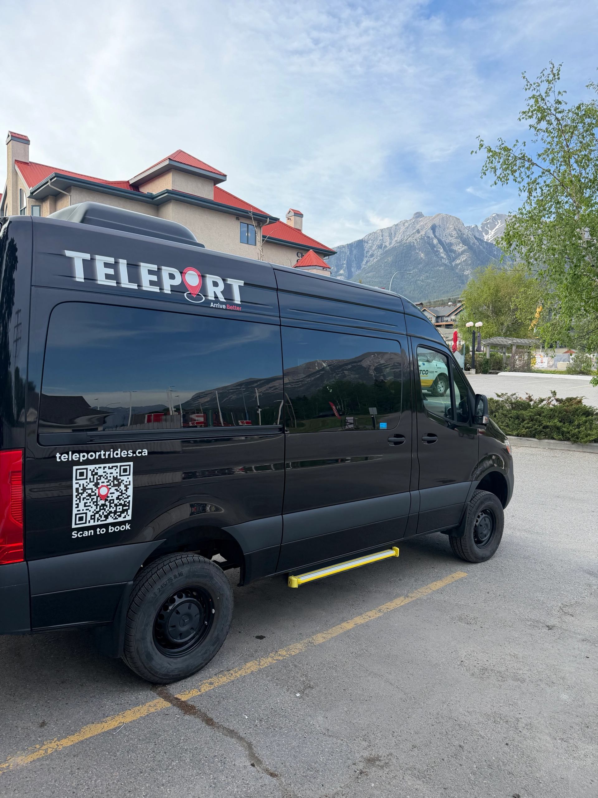 Black Teleport van with QR code parked near building and mountain backdrop.