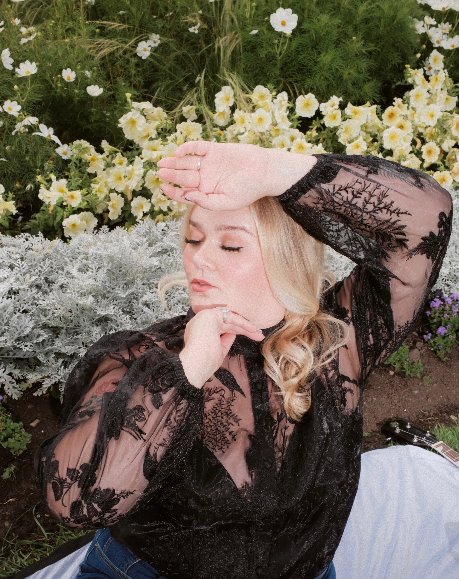 Person in black lace top poses on blanket in garden with white flowers.