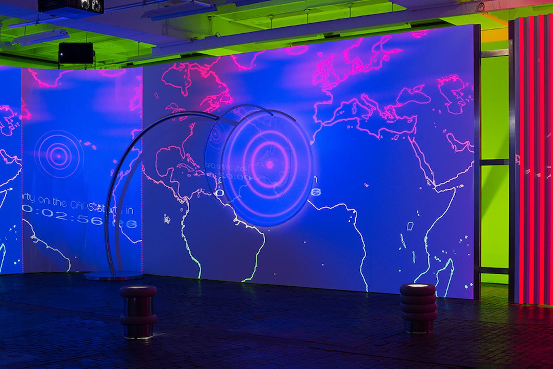 Large digital world map projection with neon outlines and circular radar graphic on wall.