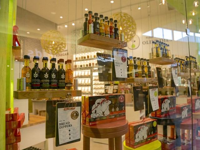 Store window with gourmet oils and boxed products on suspended shelves.
