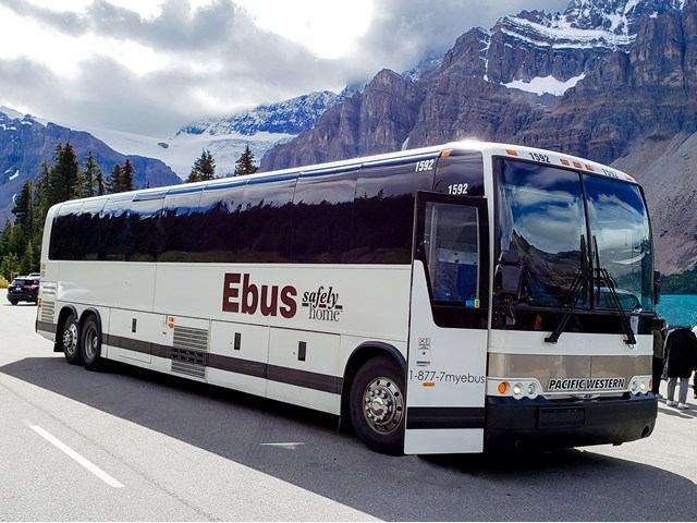 Ebus parked near lake, trees, and peaks.