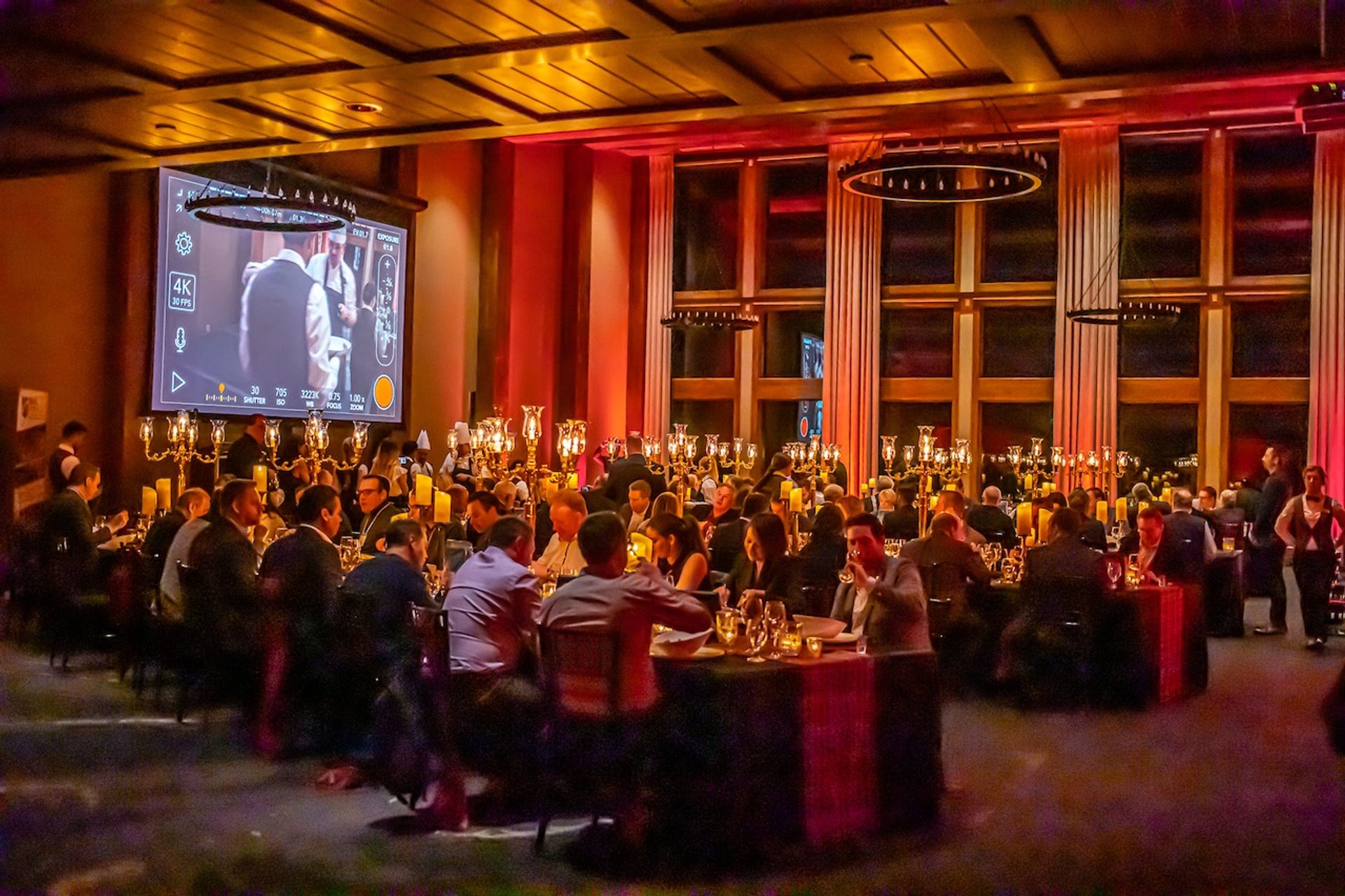 Large banquet room with candlelit tables and a projected presentation