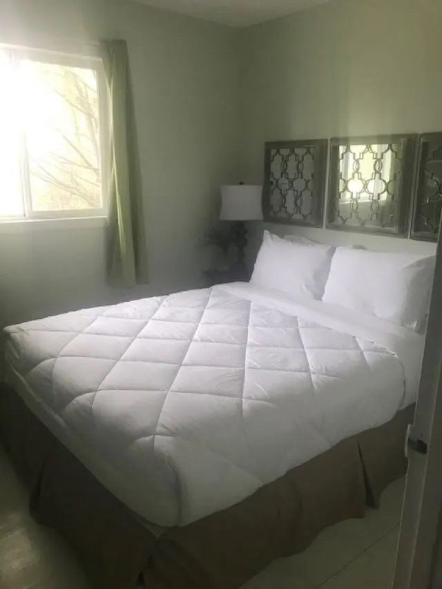 Small bedroom with large white bed, window with green curtain, and wall mirrors.