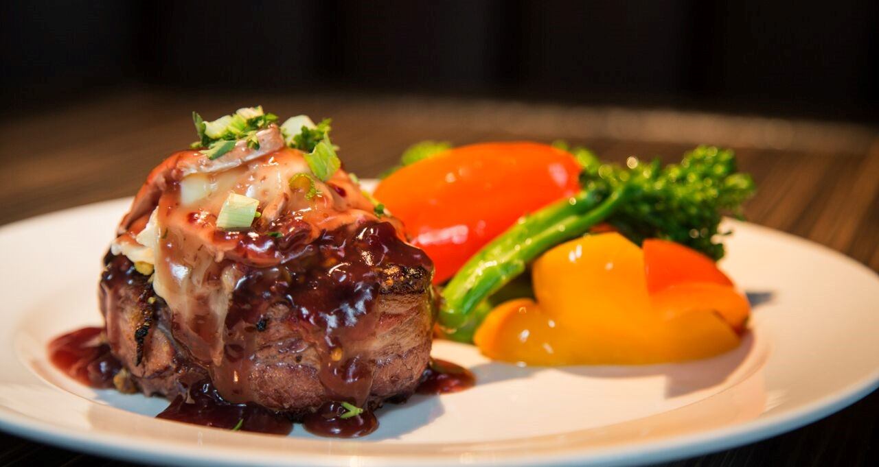 Plated meat dish with sauce, herbs, and colorful vegetables.