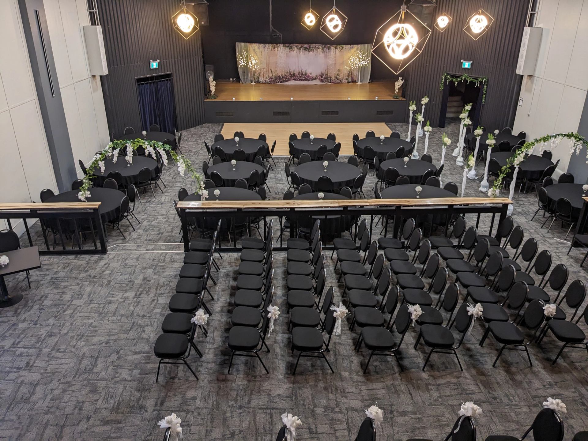 Event hall with rows of chairs, round tables, floral arches and decorated stage.
