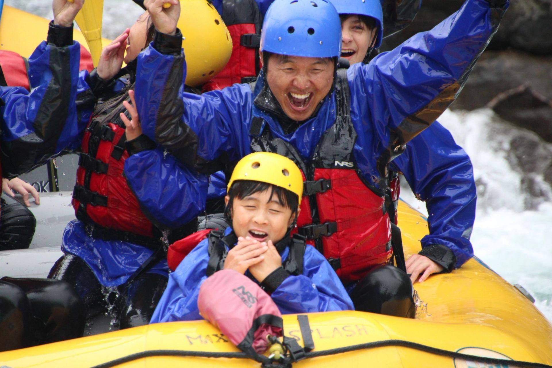 Group in helmets and lifejackets rides yellow raft through whitewater rapids.
