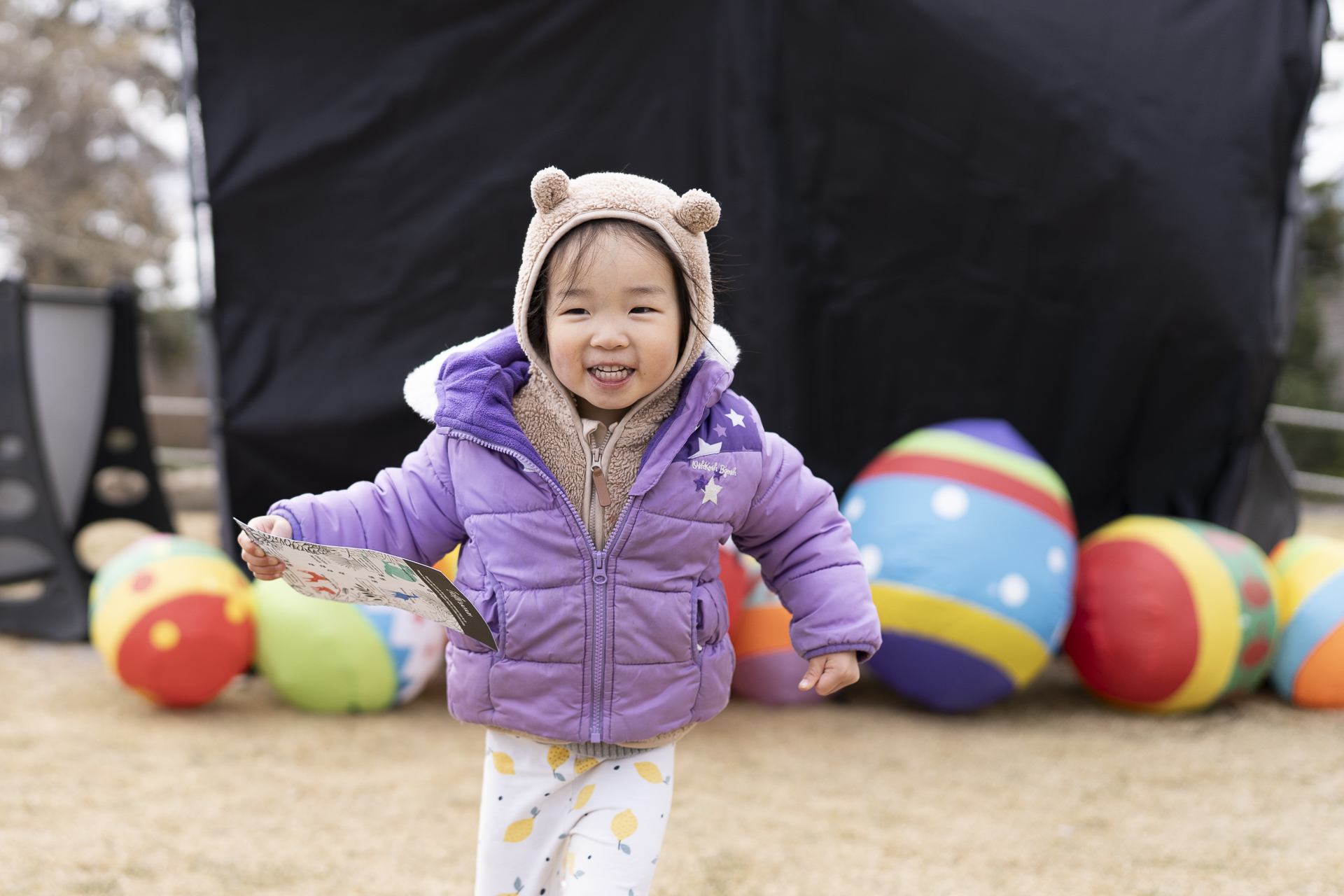 Child in a purple coat walking past large colorful Easter egg props
