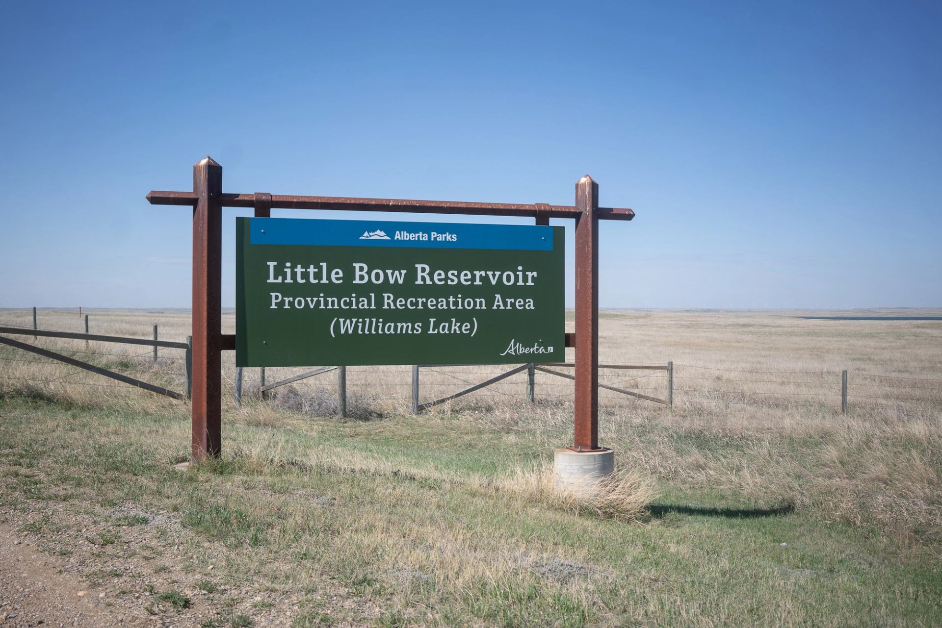 Green entrance sign for Little Bow Reservoir Recreation Area under blue sky.