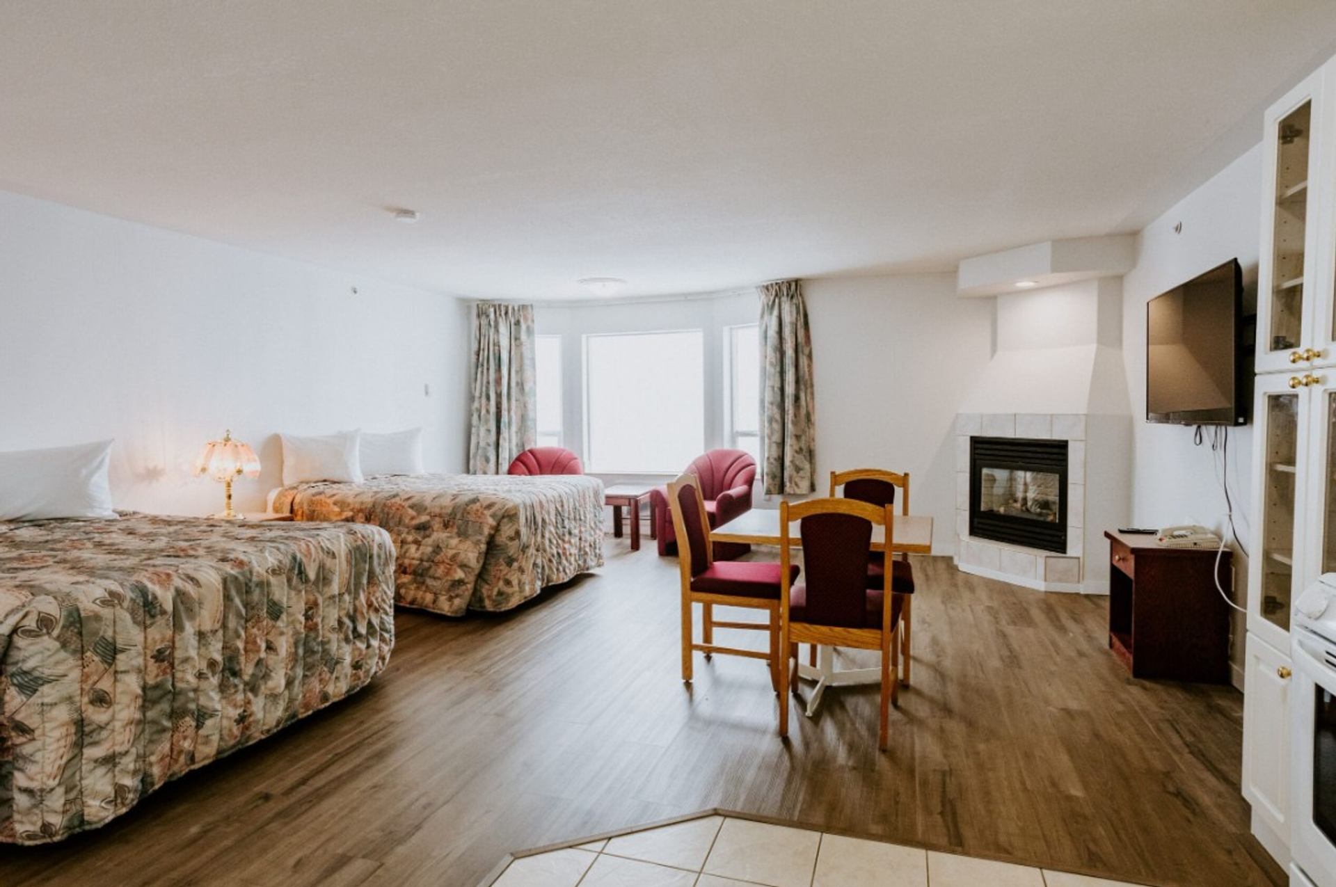 Hotel room with two beds, sitting area, dining table, fireplace and wall-mounted TV.